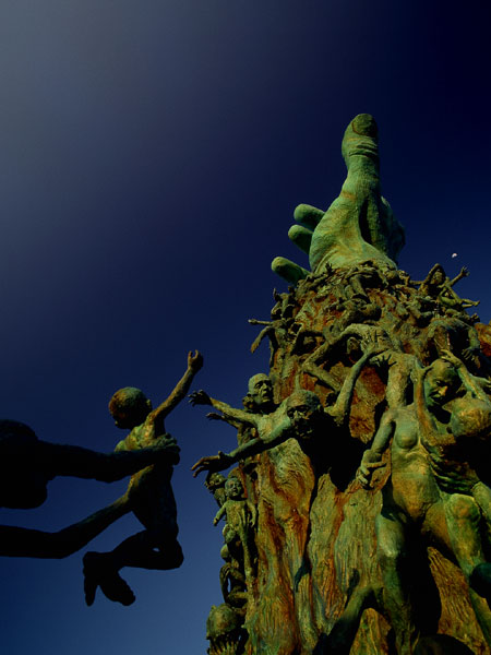 <strong>The Sculpture of Love and Anguish</strong> The towering arm rises from the center to anchor the entire work. The arm bears more than 100 intertwined figures, each portraying its own testimony. It is encircled by other freestanding victims.